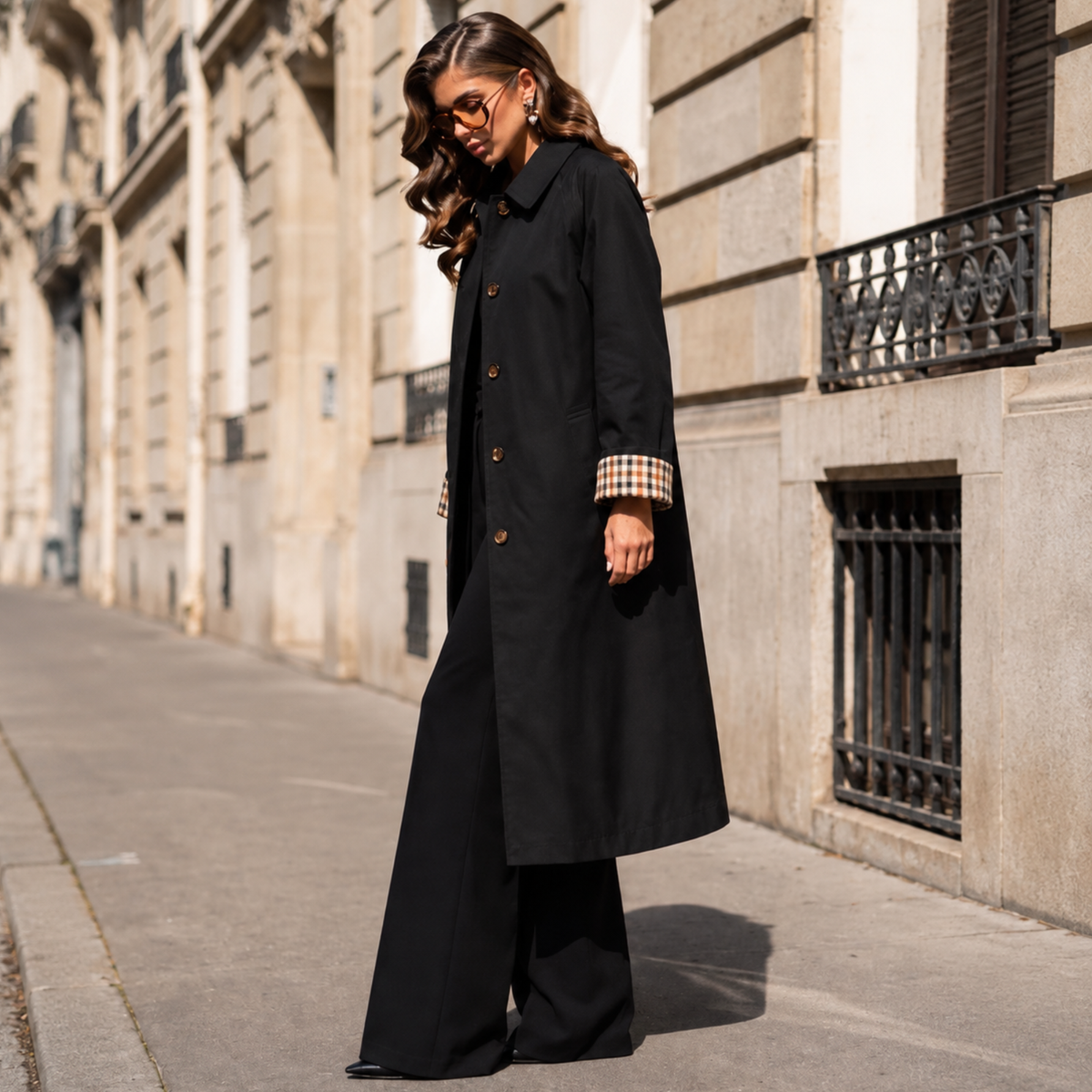 Femme portant un trench long noir avec revers de manches à carreaux.