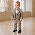 Bébé garçon portant un costume de cérémonie taupe avec gilet, nœud papillon et chemise blanche plissée