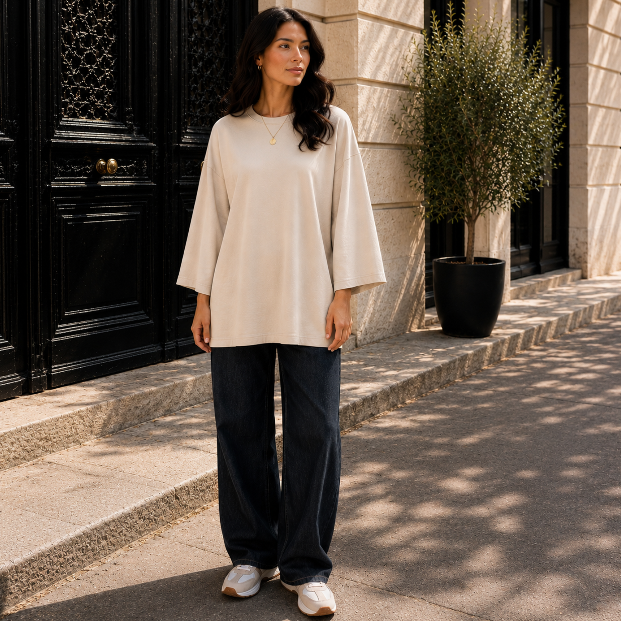Femme portant un T-shirt long oversize beige, manches longues 7/8, avec un jean large.