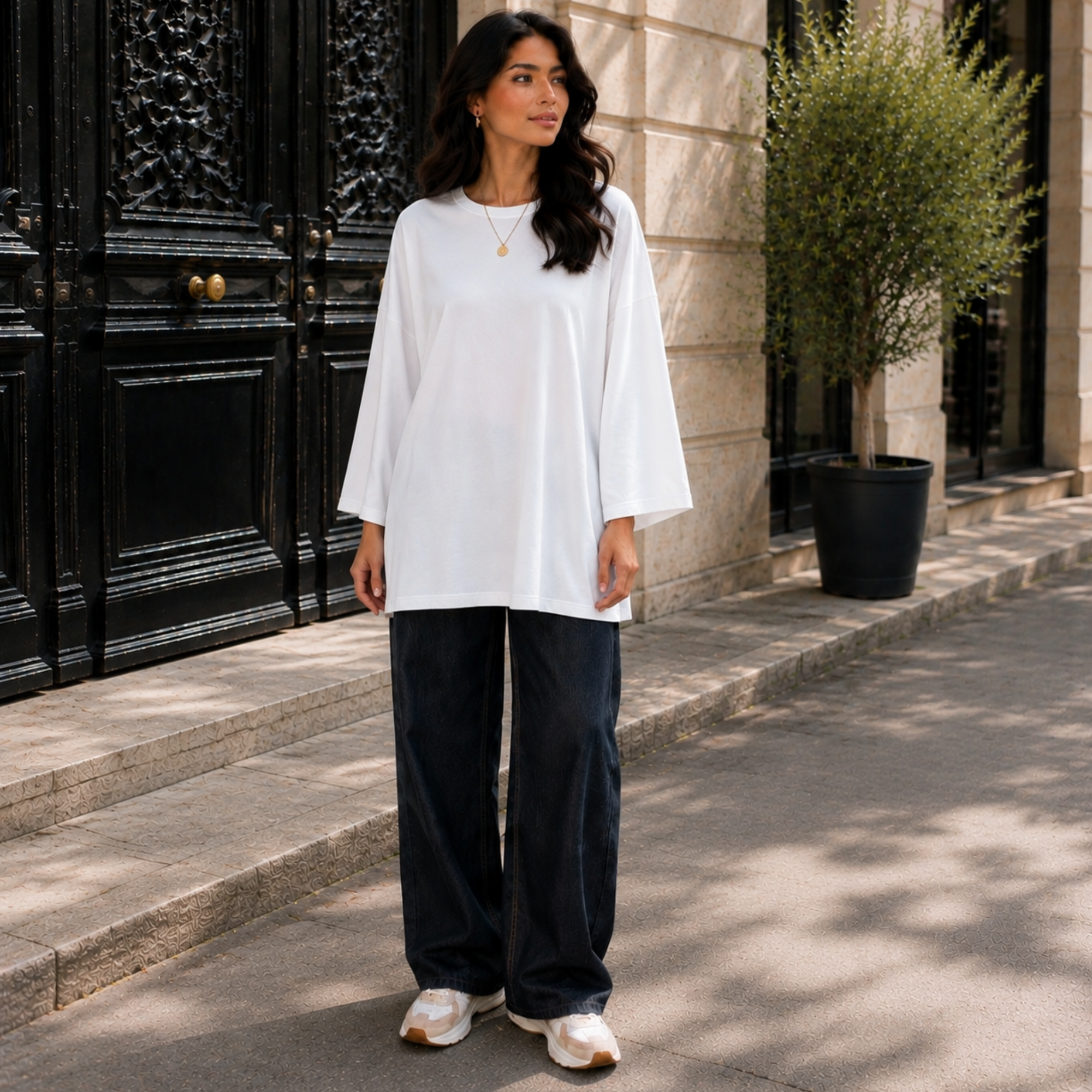 Femme portant un T-shirt long oversize blanc, manches longues 7/8, avec un jean large.