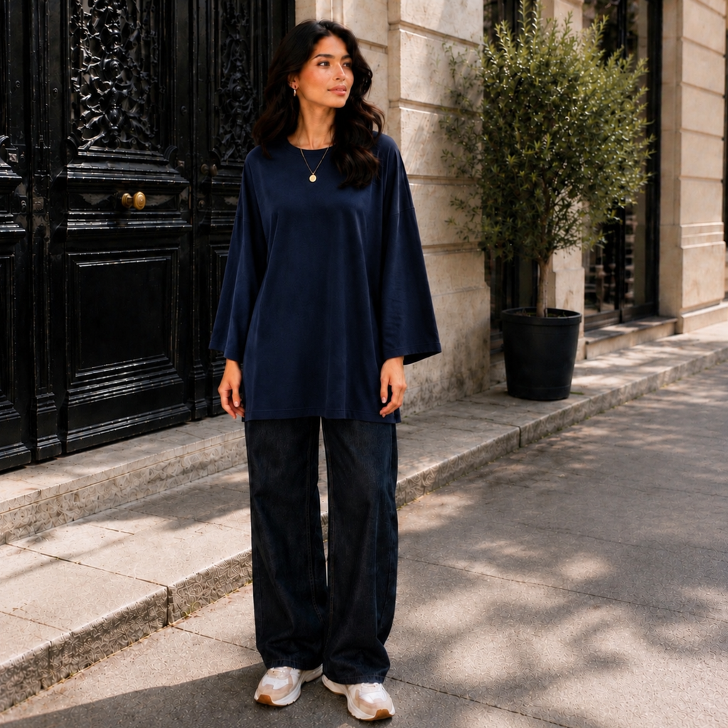 Femme portant un T-shirt long oversize bleu marine, manches longues 7/8, avec un jean large.