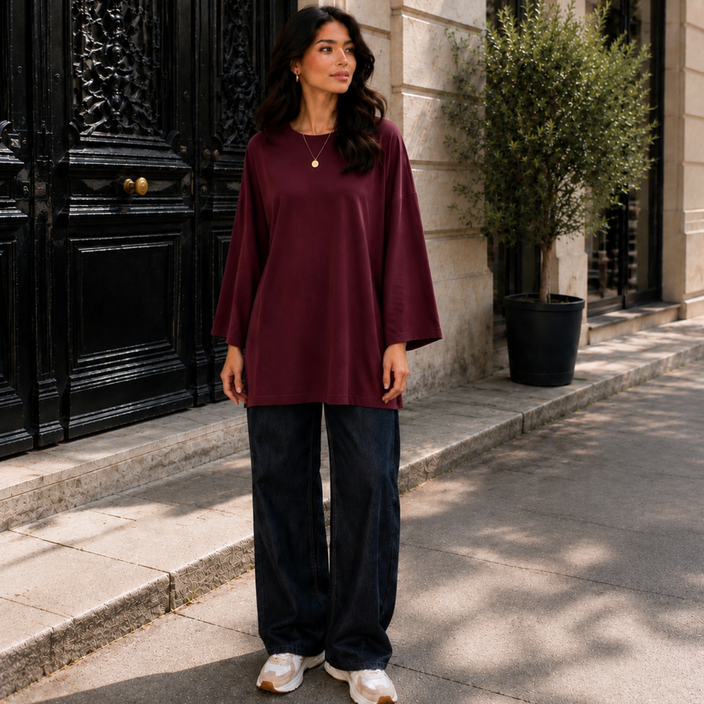 Femme portant un T-shirt long oversize bordeaux, manches longues 7/8, avec un jean large.