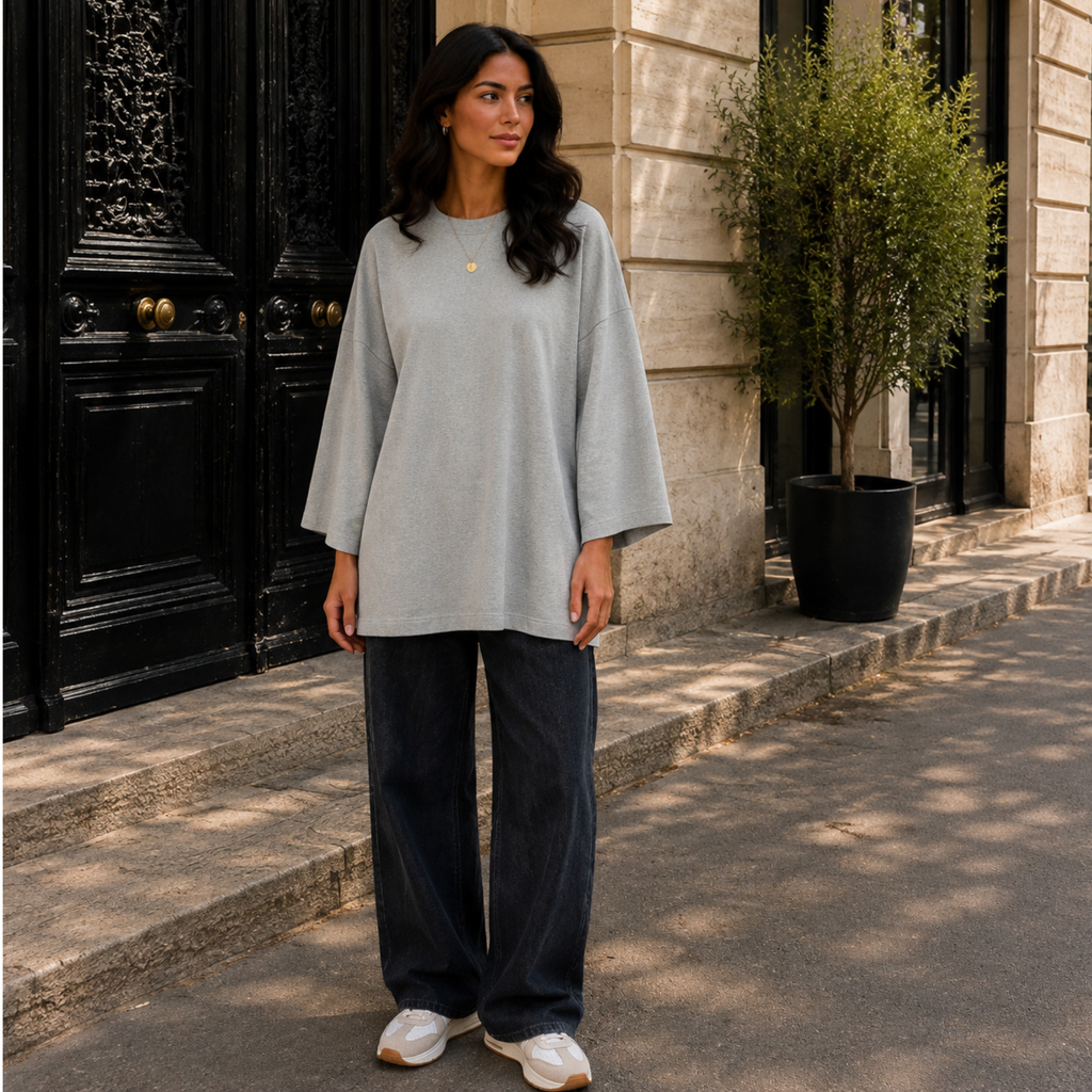 Femme portant un T-shirt long oversize gris clair, manches longues 7/8, avec un jean large.