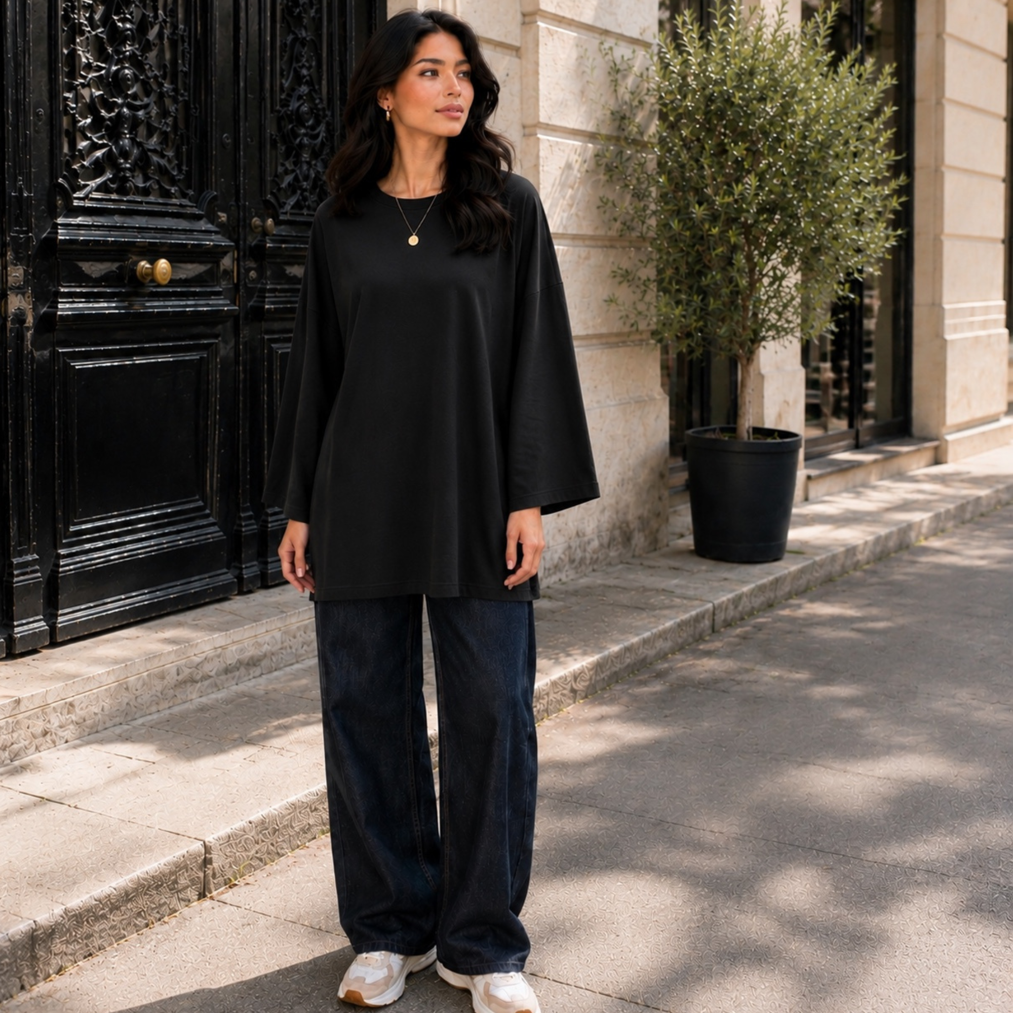 Femme portant un T-shirt long oversize noir, manches longues 7/8, avec un jean large.