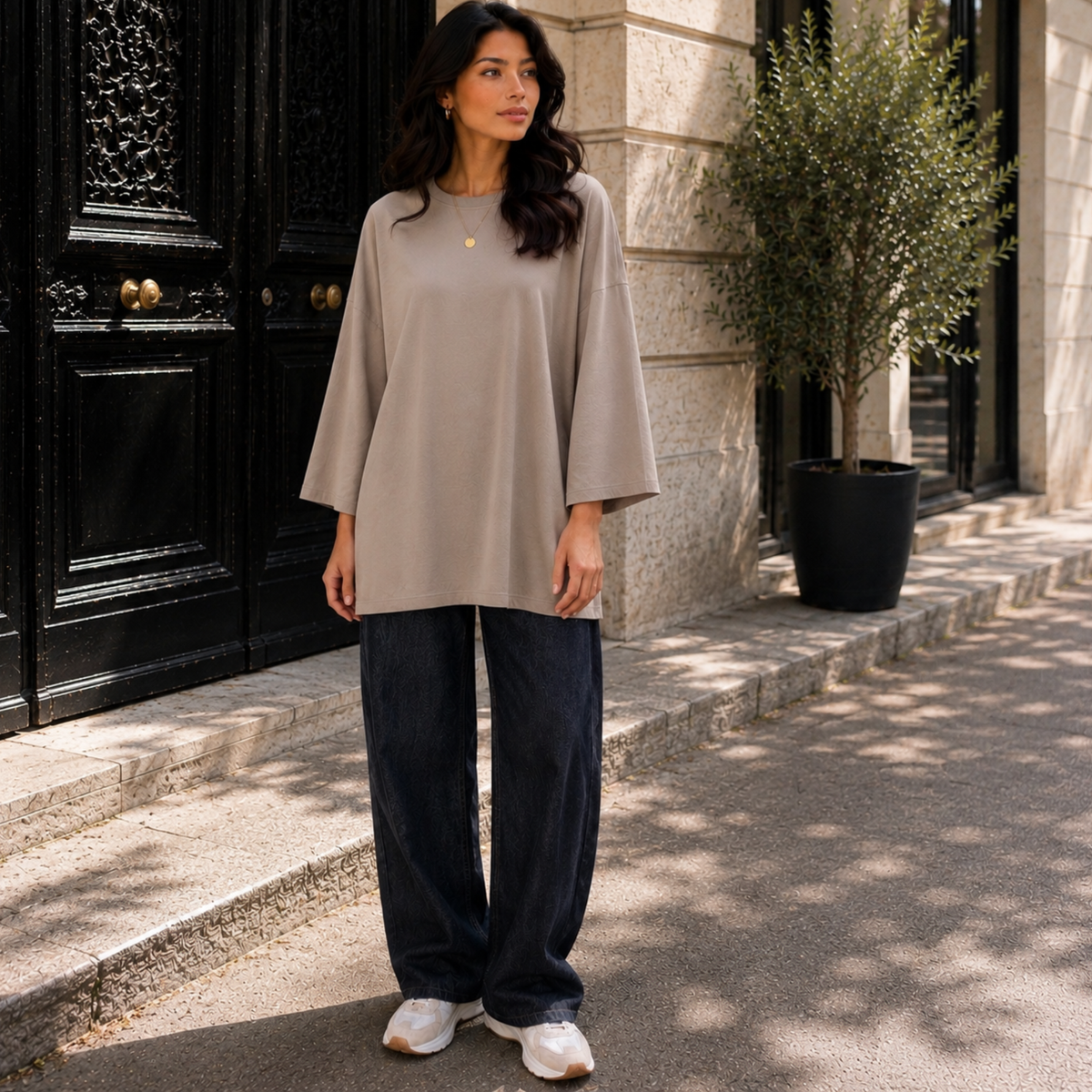 Femme portant un T-shirt long oversize gris, manches longues 7/8, avec un jean large.